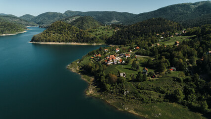 Fototapeta premium A peaceful village on the green hillside by the turquoise Zaovine Lake in spring, surrounded by forested mountains. Tara National Park, Serbia during springtime