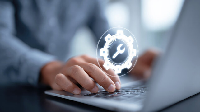 Close-up of hands on laptop keyboard with digital gear and wrench icon representing software development, system maintenance, IT support and technology services.