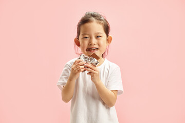 Happy Kid Girl Eating Greedily Big Chocolate Bar Isolated on Pink Background