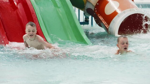 Two children boys sliding down water slide in kiddie pool. Summer vacation concept.
