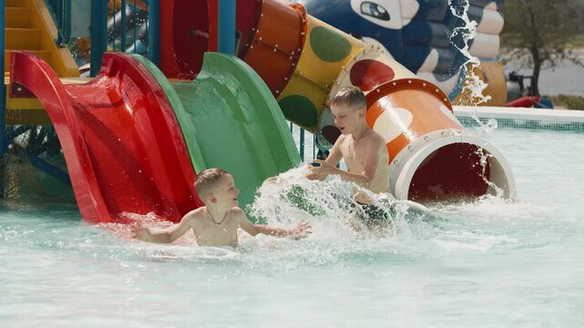 Two children boys sliding down water slide in kiddie pool. Summer vacation concept.
