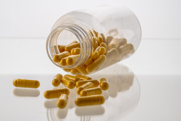 A jar with pills inside lies on a white background with reflection. Hyaluronic acid, collagen,...