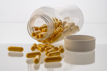 A jar with pills inside lies on a white background with reflection. Hyaluronic acid, collagen,...