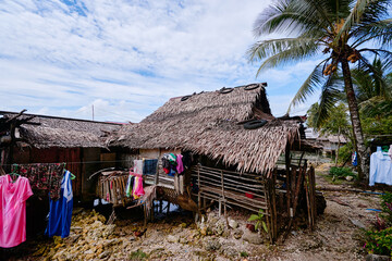 A humble thatched hut located in a tropical coastal setting with laundry drying outdoors,...