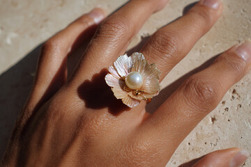 Close-up of a handcrafted seashell ring with pearl on a woman's hand
An artistic handmade ring featuring layered iridescent seashell petals and a central pearl