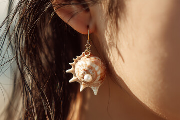 Close-up of a sea shell earring with pearl on ear
A detailed view of an elegant earring made from a real spiral sea shell, delicately hanging from a woman's ear. 