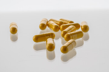 Yellow pills are scattered on a white background with a reflective surface.