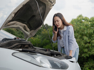 An upset woman is talking on the phone to a broken car with the hood open.