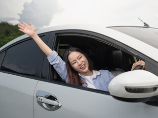 A happy Asian woman stretches her hand out of the car.