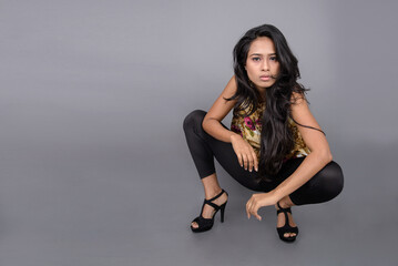 A charming young woman wearing a floral patterned top, black leggings and black heels, posing with...