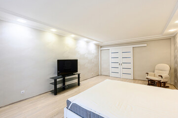 bright bedroom with a white bed, TV on a stand, sliding doors, and a rocking chair. The walls are...