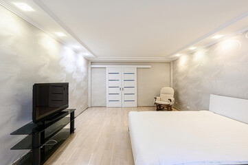Bright bedroom features a large bed, TV, sliding doors, and a rocking chair