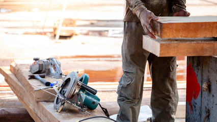 Male carpenter setting workbench preparing work tools for cutting and planing timber. Electric circular saw with planer and hammer on wooden plank at construction site. Lumber industry concept