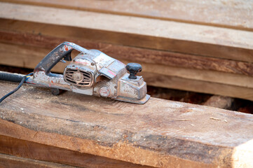 Rustic old electric planer on timber stack or wooden plank with sawdust spreading around. Work tool for carpentry. Lumber industry concept