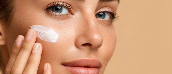 A young woman is carefully applying a cream to her face, enhancing her radiant skin. The warm background complements her beauty routine, revealing a focus on self-care and grooming.