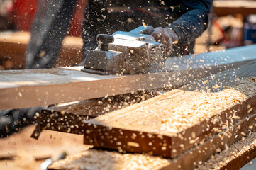 Male carpenter hand using an electric planer on wooden plank in workshop. Woodworker planing timber...