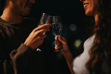 A young couple shares a joyful toast with glasses in hand during a romantic evening, smiling and enjoying each others company.