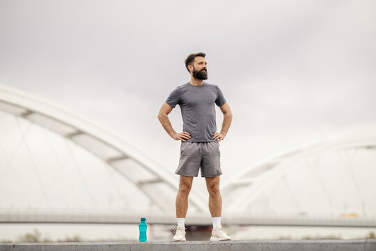 Portrait of strong sportsman standing on riverbank with hands on hips.