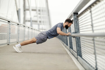 Side view of masculine strong sportsman doing pushups on a bridge.