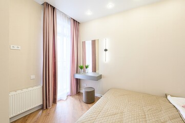cozy room with beige walls. A bed, vanity, curtains, and wood floors create a peaceful ambiance
