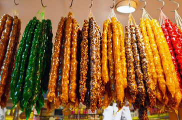 Brightly colored churchkhela hangs displayed for sale at market stall. Traditional Georgian and Turkish sweet made with nuts and grape juice, offering vibrant food background.