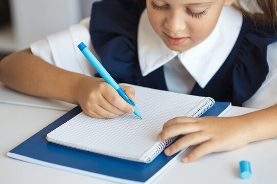 School kig writing a schoolwork in a notebook with a blue pen. Child doing homework.