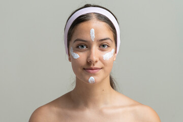 Young woman with cream dots on her face, demonstrating a skincare or makeup application routine.