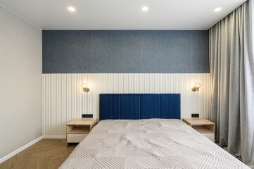 modern bedroom with a bed featuring a blue headboard and quilted cover.  The room has a two-tone wall design and minimalist bedside tables
