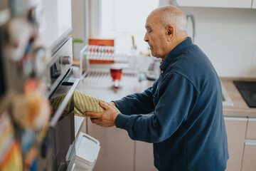 Elderly man carefully handles an oven in a bright kitchen, wearing a navy sweater and showcasing...