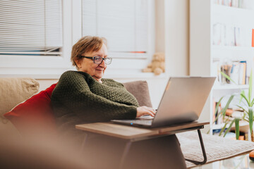 An elderly woman engaging with her laptop in a cozy living room, enjoying connection and technology in a serene home setting.