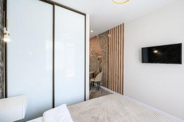 well-lit bedroom with a large closet, bed, TV, and accent wall. The room features modern décor and neutral colors