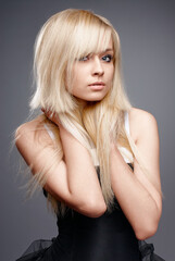 A close-up studio portrait of a young woman with long blonde hair, wearing a black outfit. The...