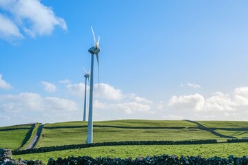 Fototapeta premium Towering Wind Turbines on Green Rolling Hills Under Blue Azorean Sky. Sustainable Energy, Renewable Power, Lush Landscape, Eco Friendly