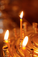 Burning thin orthodox church candles in golden holders, glowing warmly in a religious or ceremonial...