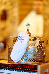 Ornate golden wedding crown with white embroidered cloth in Orthodox church setting, symbolizing traditional religious marriage ceremony.