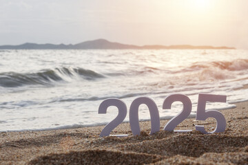 number 2025 on sandy beach with sea ripple wave at background with golden sun light during sunset time