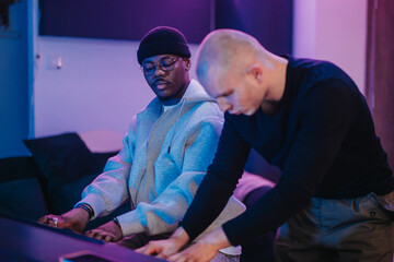 Musicians working together in a recording studio, focusing on the digital keyboard. The ambient lighting sets a creative mood, highlighting the teamwork and passion involved in collaborative creation.