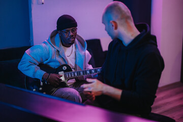 A person receives a music lesson on an electric guitar in a dimly lit room. The ambiance adds to...