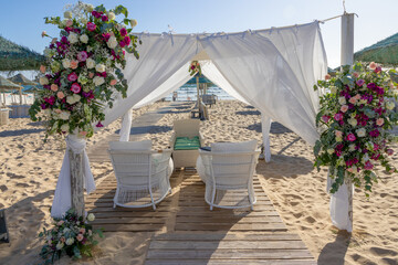 Floral canopy and seating await wedding ceremony on sandy beach