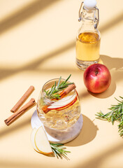Apple cocktail or cider in a glass with ice, cinnamon and rosemary on a marble stand