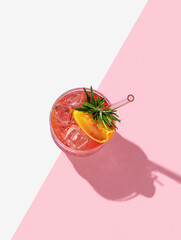 Blood orange cocktail with ice and rosemary on a pink white background with shadows.