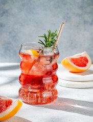 Lemonade with grapefruit, rosemary and ice in a glass on a light background with sunlight. © Kufotos