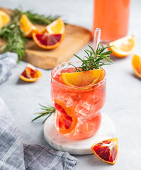Blood orange cocktail with ice and rosemary  on a light background with citrus fruits and napkin.