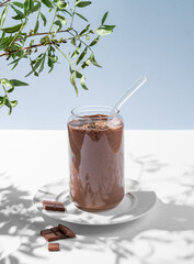 Chocolate smoothie with banana in a glass on a white blue background with morning shadow