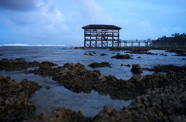 A scenic elevated pavilion sits atop wooden pillars in a coastal area with rocky shores. The serene...