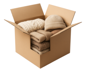 Cardboard box filled with neatly folded beige sweaters and a knitted hat on transparent background.