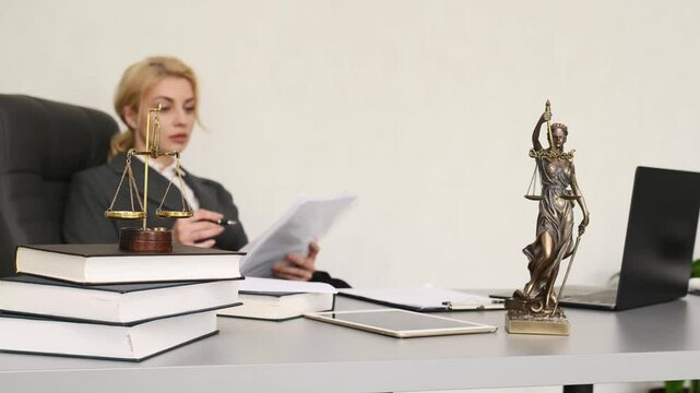 Professional woman in gray suit working with legal documents at office desk, Lady Justice scales symbolizing fairness and law in foreground, concept of legal expertise, justice, professional authority