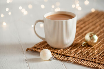 A white cup with hot coffee or tea on a white wooden table with Christmas lights.