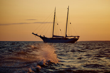 The silhouette of an ancient frigate in the sea at sunset, splashes of waves illuminated by the sun