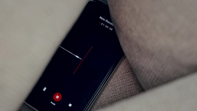 Phone secretly recording conversation hidden between pillows listening covertly. Smartphone eavesdropping or covert investigation with surveillance gathering conversation or evidence using digital app